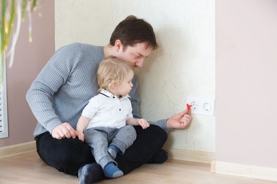 Father covering outlet while baby watches
