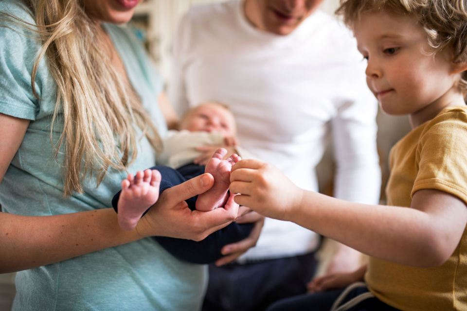 Mother holding newborn while son touches newborns foot