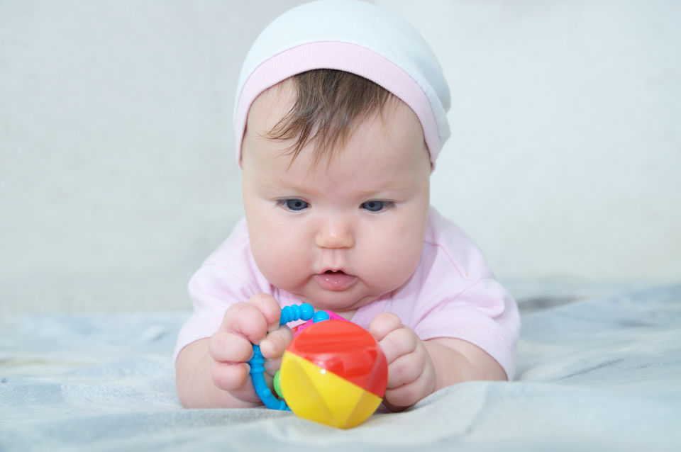 Bebita con gorro rosa mira un juguete