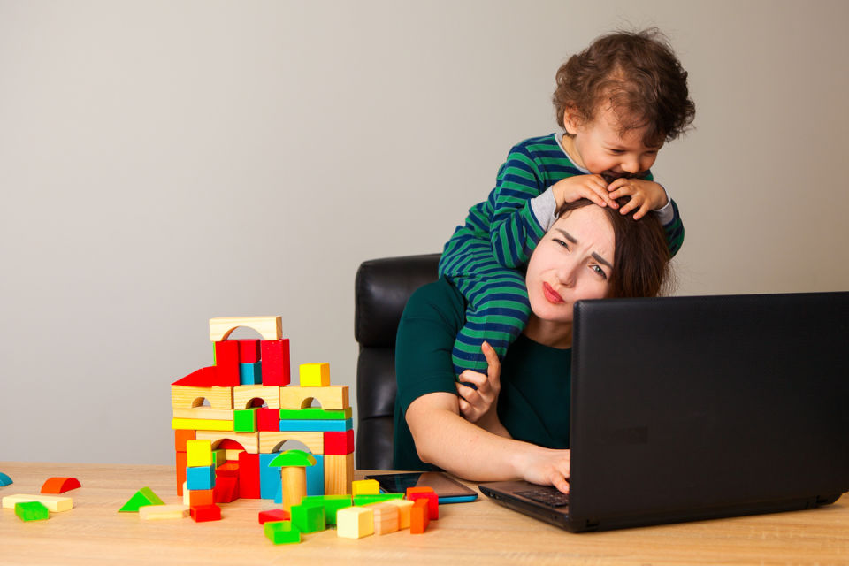 Son climbing on mothers head while she works on computer 