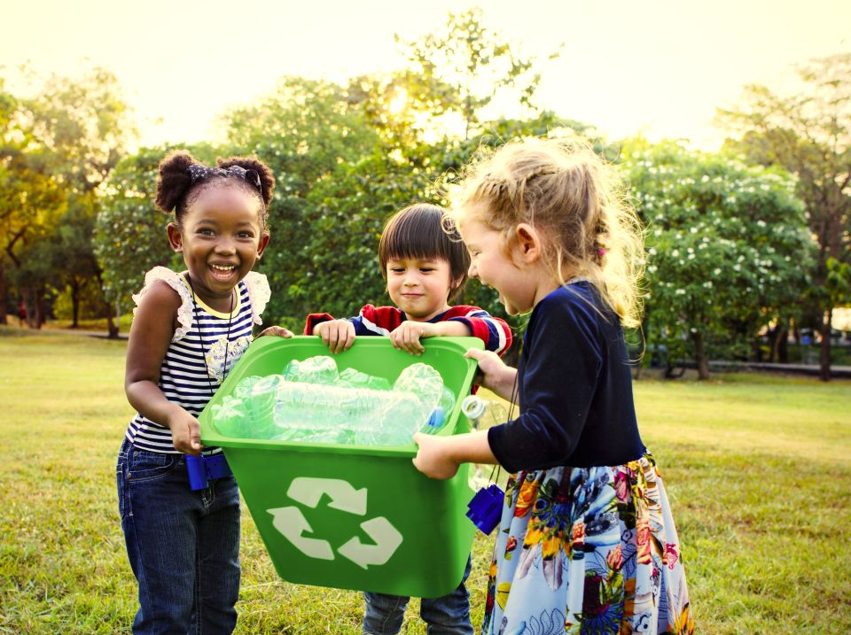 Tres pequeños en el parque sosteniendo un contenedor de reciclaje