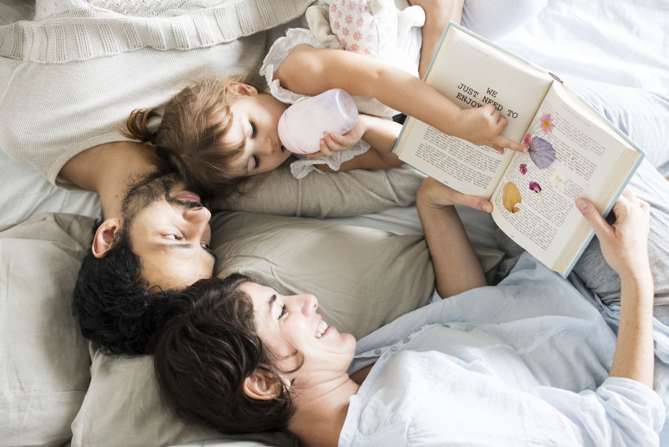 Parents laying in bed reading to daughter