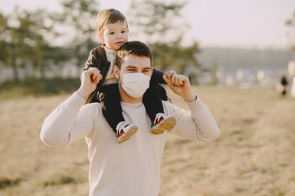 Father with face mask carrying son on shoulders