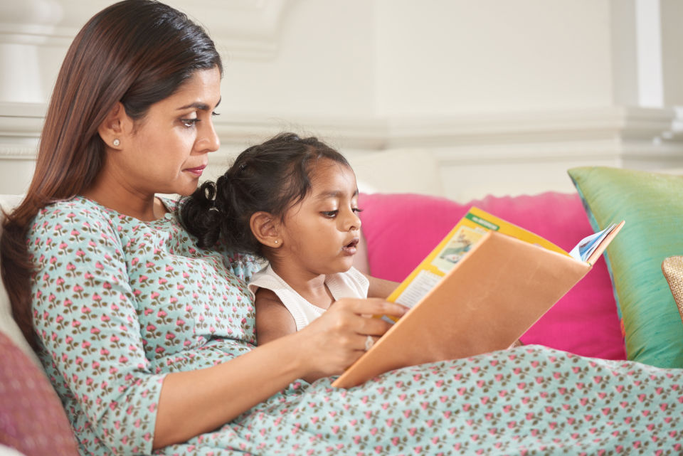 Mother and Daughter laying down reading a book on couch
