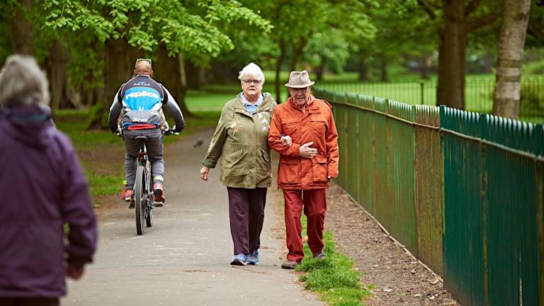 Old couple walking arm in arm in a park