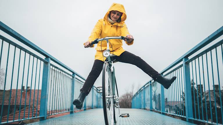 Lets go ride a bike! Young woman in bright yellow raincoat having fun riding a bike