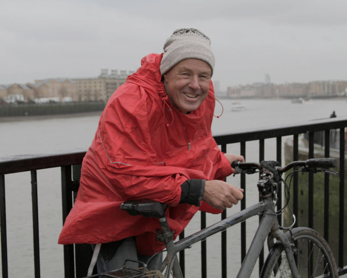 Man wearing a raincoat standing in the rain by his bike