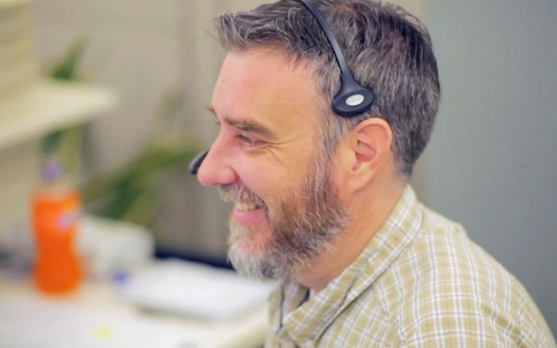 CX Rep with Headphones Smiling at Computer Screen