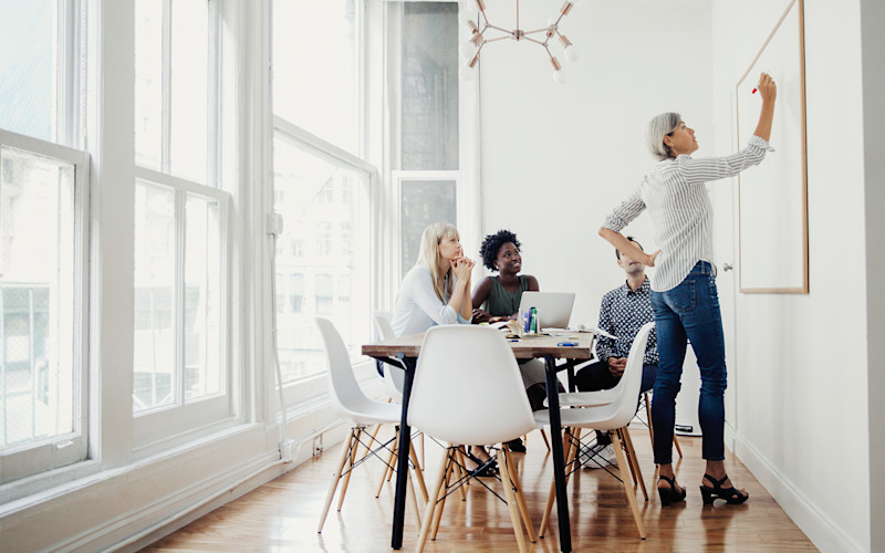 L woman at whiteboard with three coworkers