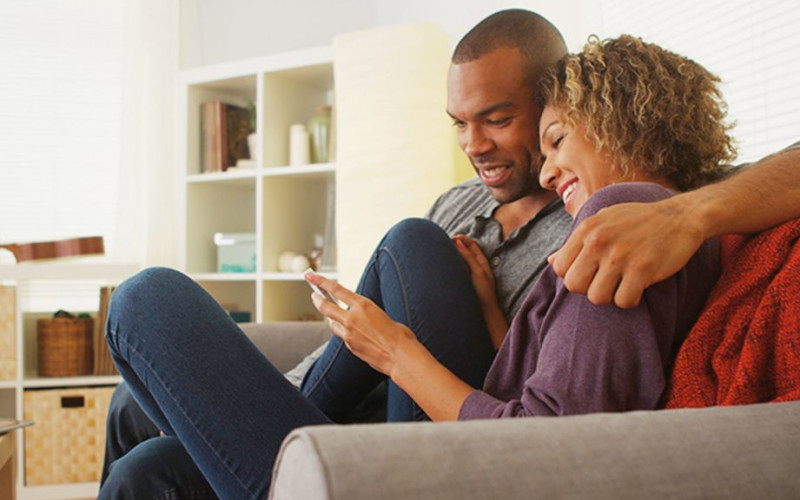 L couple cuddling on couch looking at mobile phone