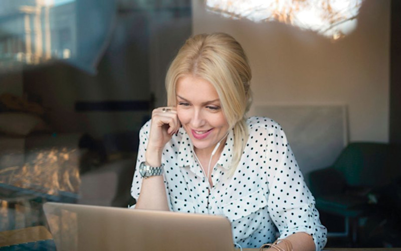 L female smiling at laptop earbuds coffee shop