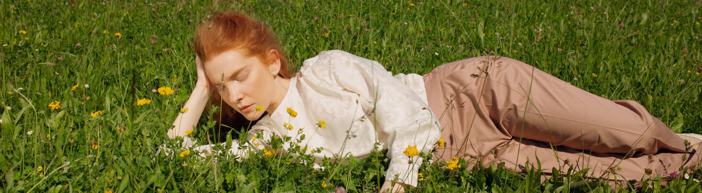 Pistil product image, lady with red hair lying down in field with yellow flowers