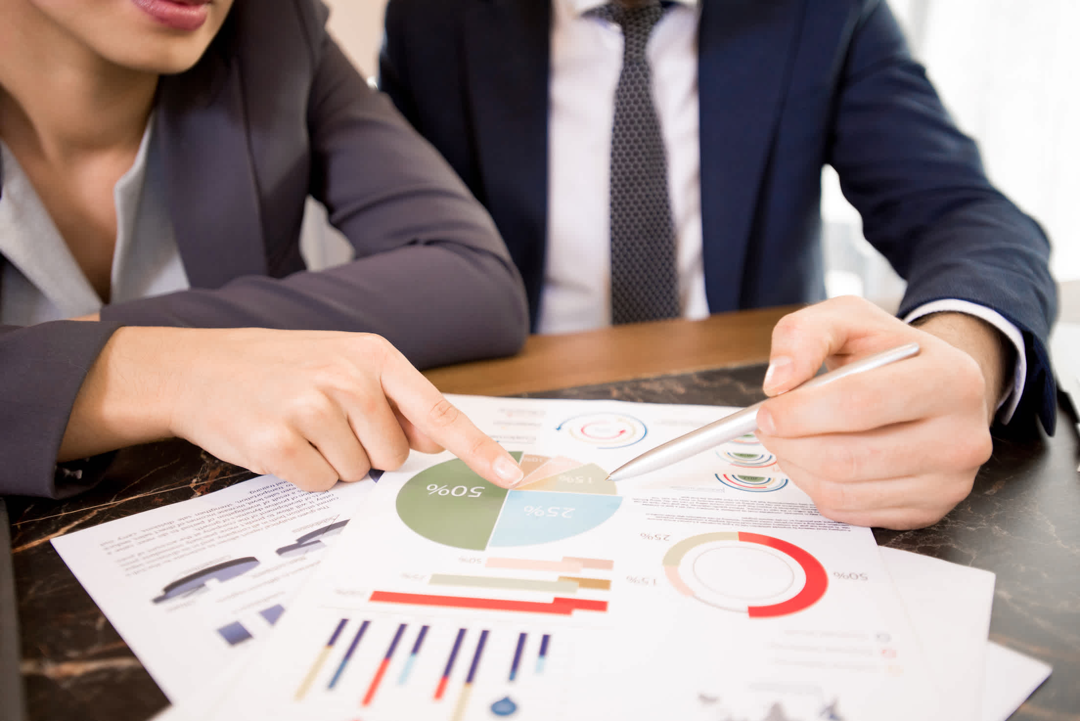 Close-up of unrecognizable business analyst viewing survey report and discussing results of research at table, woman pointing at pie chart