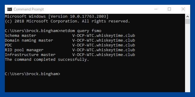 Command prompt output of "netdom query fsmo" showing all five FSMO roles assigned to a single domain controller.
