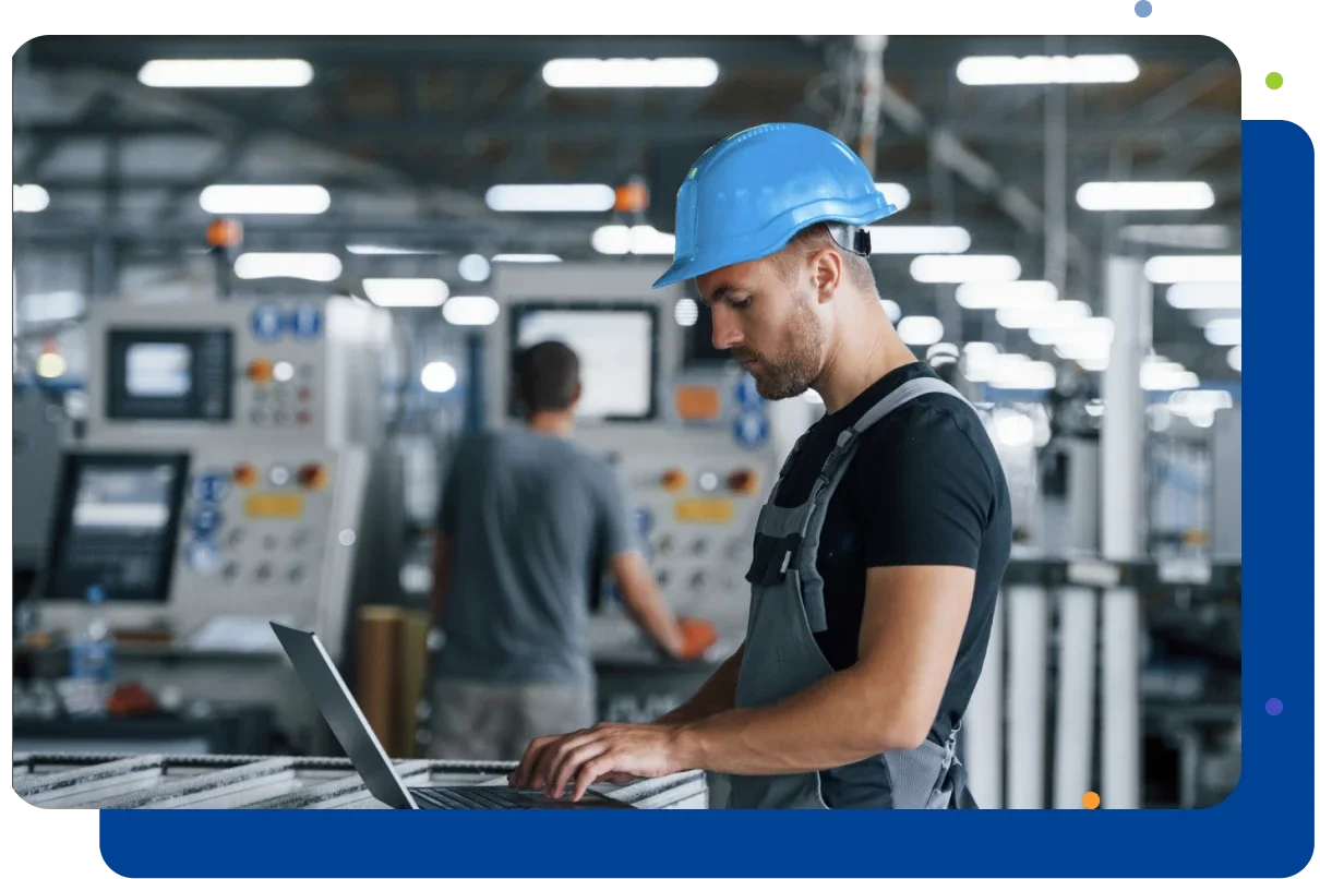 Man wearing a hardhat working on a laptop in a factory