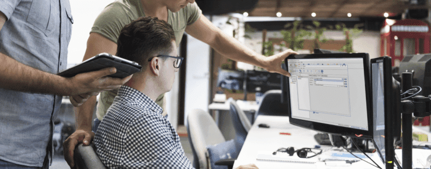 Group of men looking at computer with PDQ Deploy screen