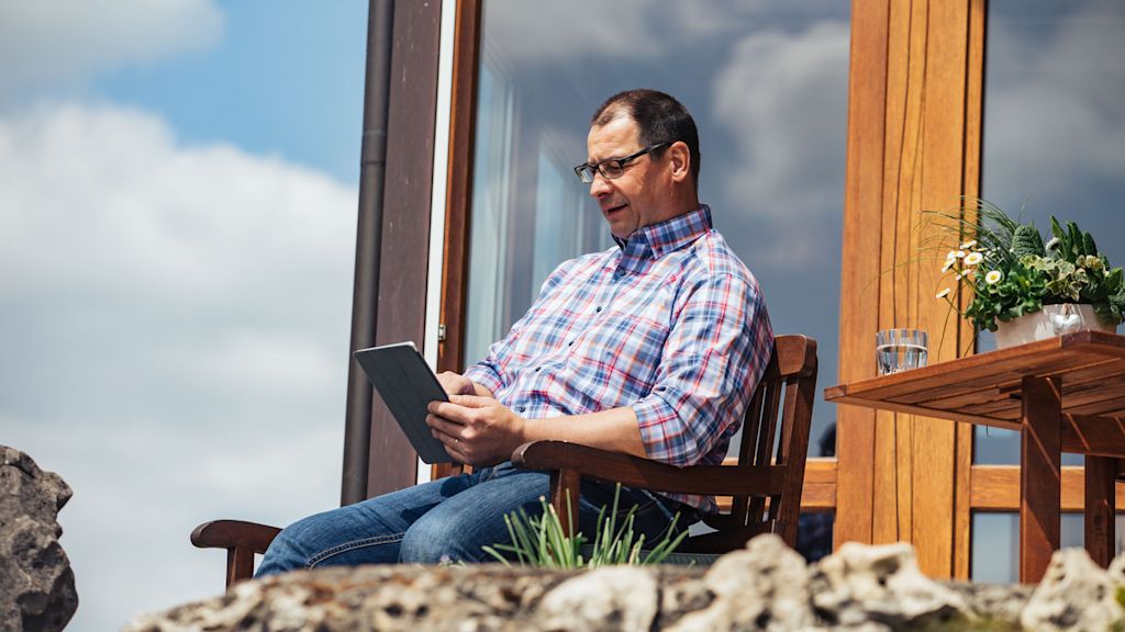 Mann sitzt vorm Haus und guckt auf sein Tablet.