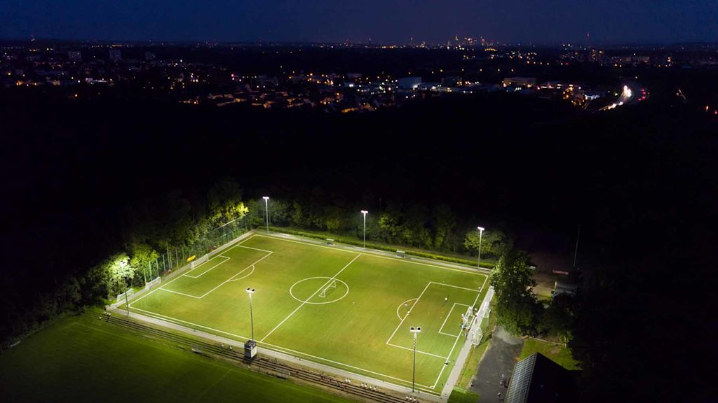 Beleuchteter Fußballplatz bei Nacht von oben.