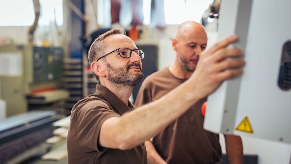 Zwei Männer bedienen eine Maschine in einer Werkstatt.