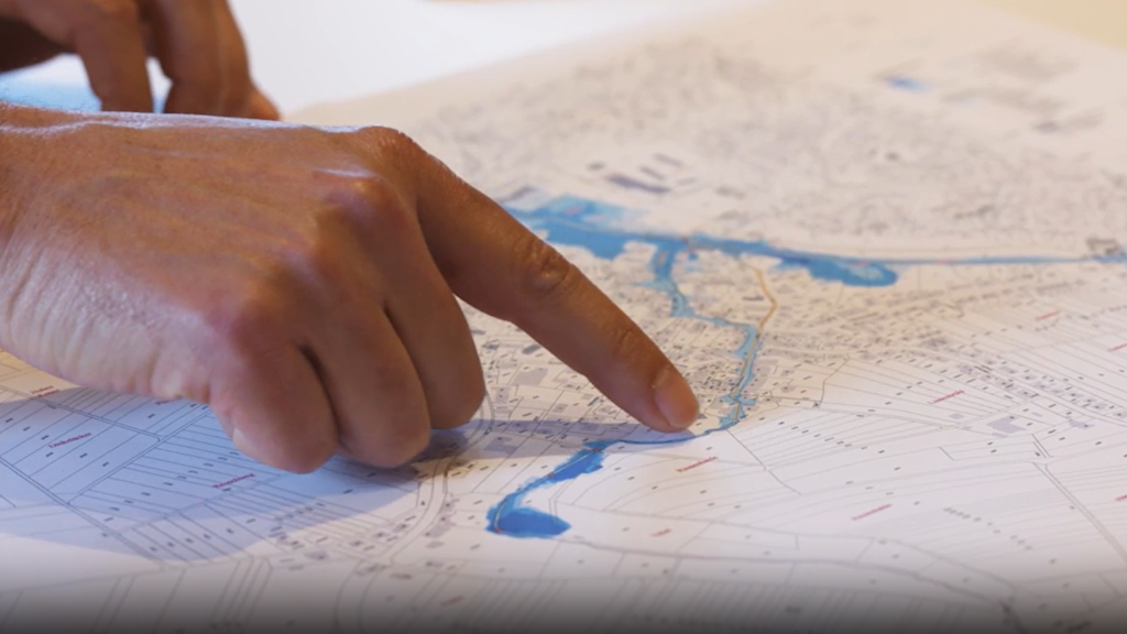 Hand zeigt auf Überschwemmungsgebiet auf Karte.