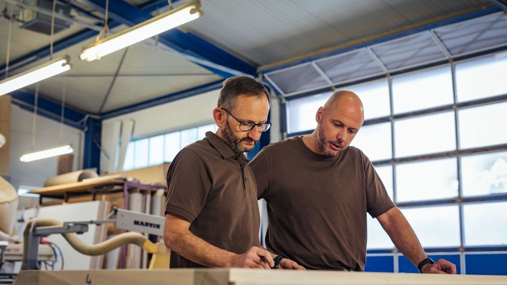 Zwei Männer besprechen in einer Werkstatt Pläne.