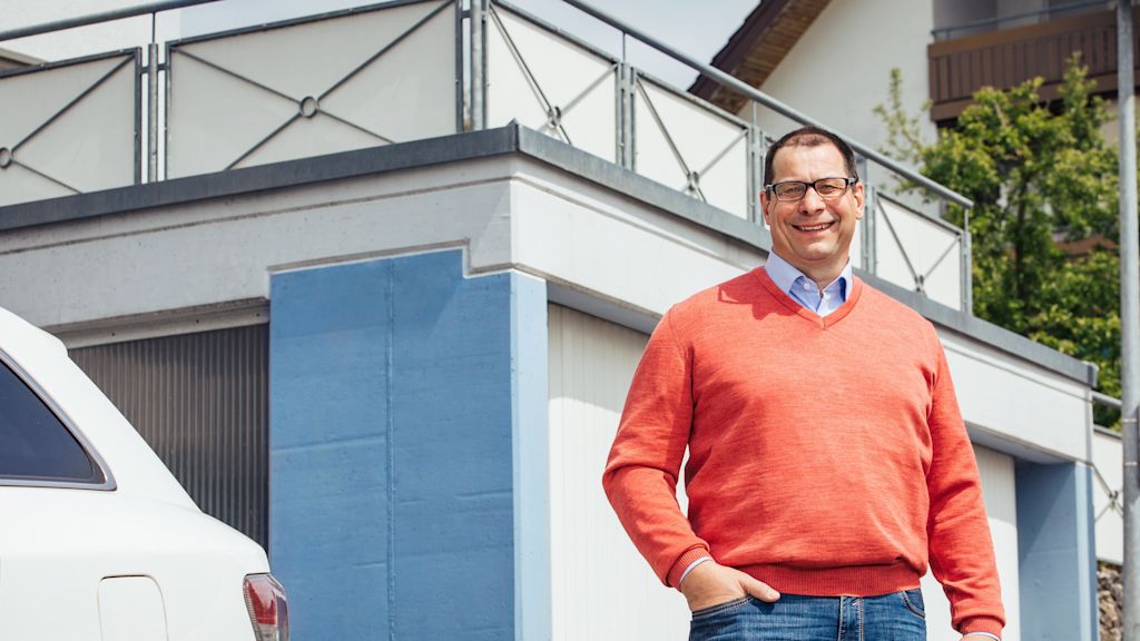 Mann lächelt vor Haus mit Garage.