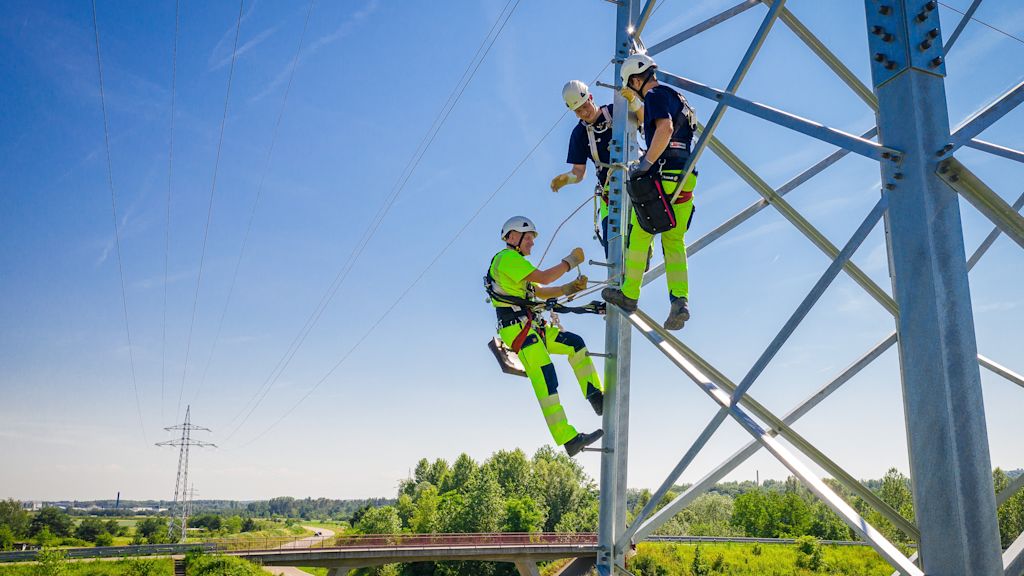 Drei Monteure arbeiten an einem Hochspannungsmast.