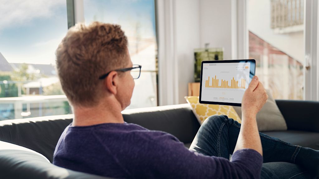 Mann sitzt auf Sofa, betrachtet Tablet mit Diagramm.