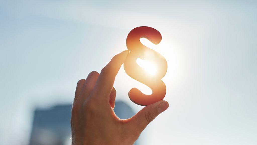 Hand hält Paragraphenzeichen vor Sonne.