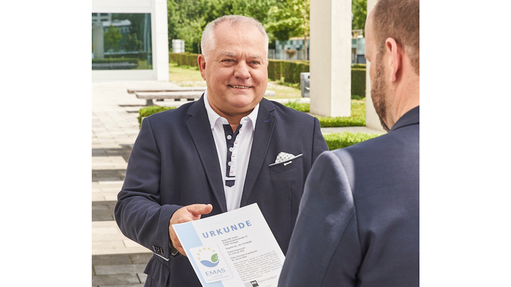 Mann in Anzug überreicht einem anderen Mann eine Urkunde.