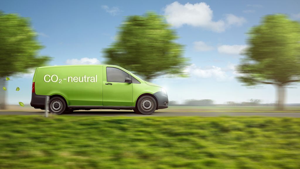 Grüner Lieferwagen mit Aufschrift "CO2-neutral" fährt durch grüne Landschaft.
