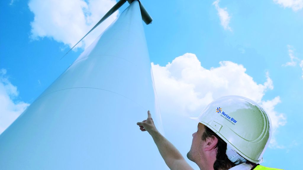 Arbeiter zeigt von unten auf Windkraftanlage.