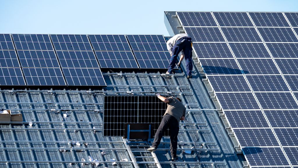 Zwei Arbeiter montieren Solarmodule auf einem Dach.