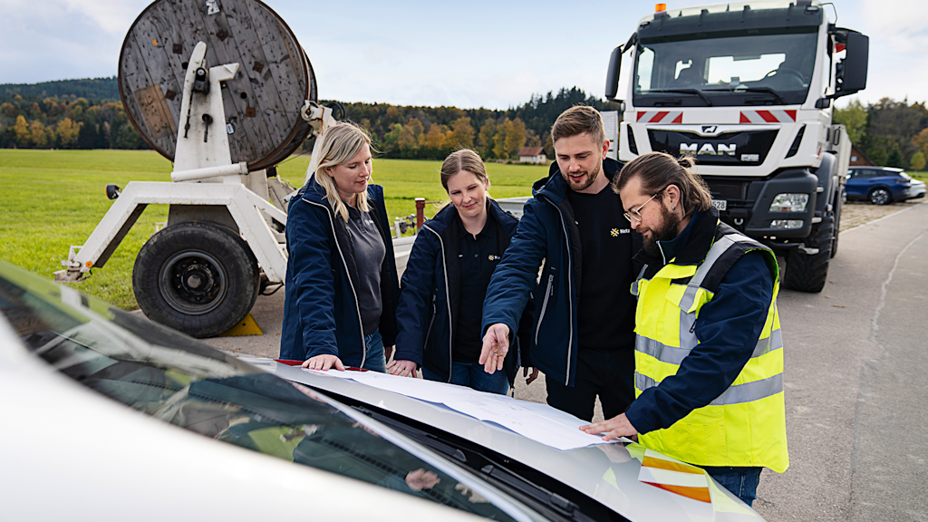 Vier Personen besprechen Pläne auf einer Motorhaube.