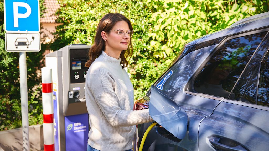 Frau lädt E-Auto an Ladesäule.