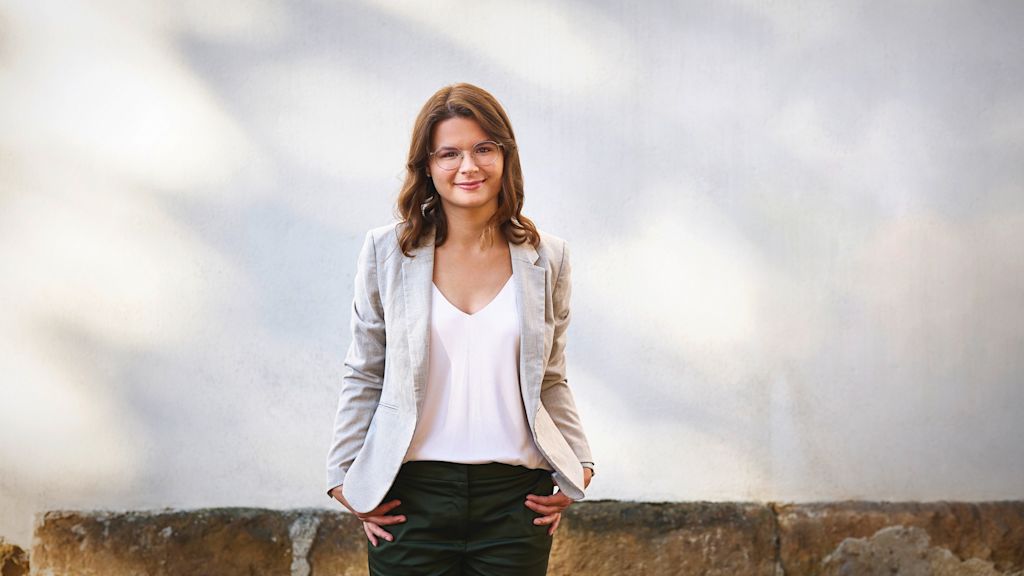 Lächelnde junge Frau mit Brille und im beigen Blazer.