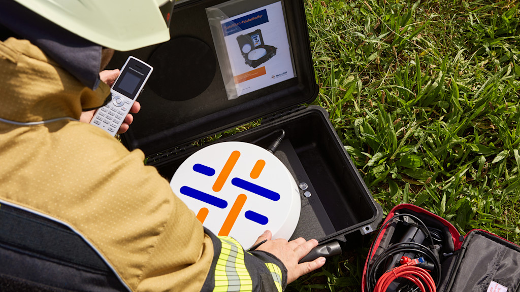 Transportkoffer für Satellitenkommunikation liegt geöffnet im Gras, Monteur kniet davor.