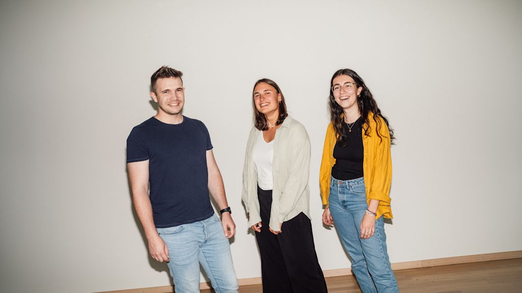 Drei junge Menschen lächeln vor weißem Hintergrund.