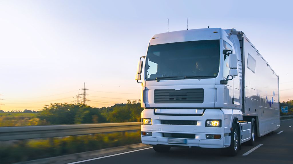 Weißer LKW fährt auf Autobahn, Strommasten im Hintergrund.