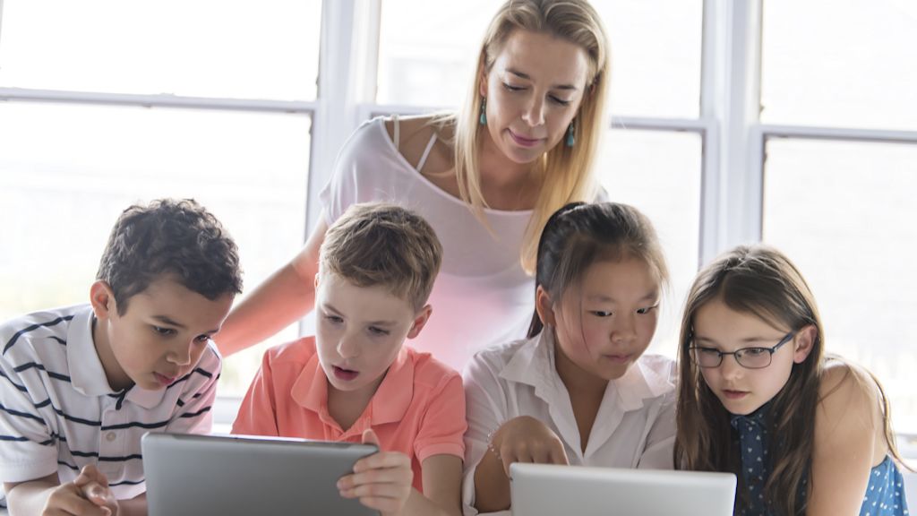 Lehrerin hilft Schüler*innen bei der Arbeit an Tablets.
