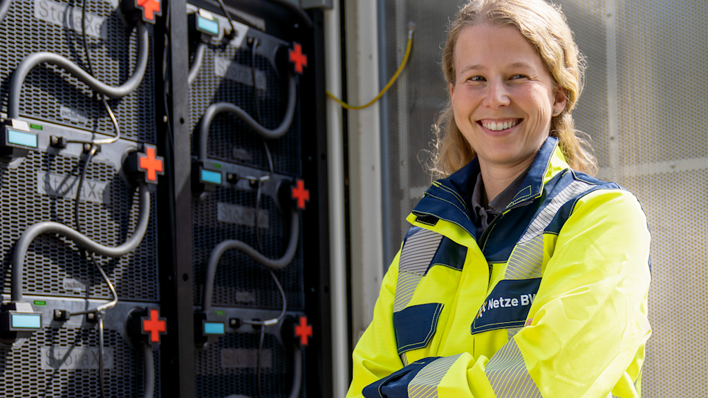 Frau lächelt vor Batteriespeicher.