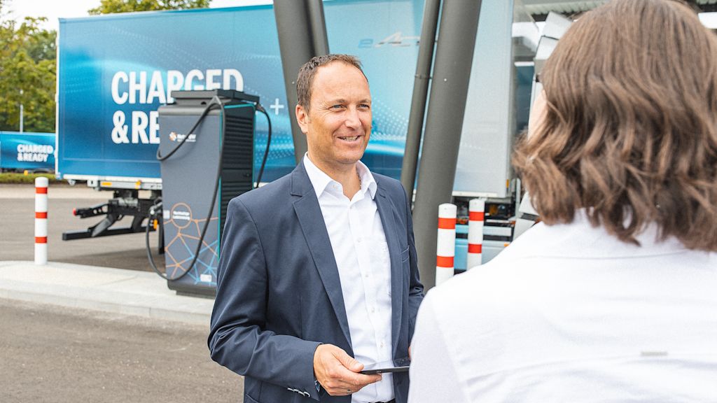 Lächelnder Mann im Anzug vor Ladesäule für E-LKW.