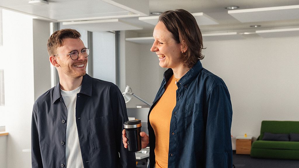 Zwei Trainees der Netze BW GmbH stehen in den Büro Räumen der Netze BW GmbH und lächeln sich zu.