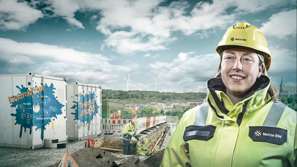 Frau in Netze BW Arbeitskleidung steht vor einer Baustelle für eine Elektrolyseanlage.