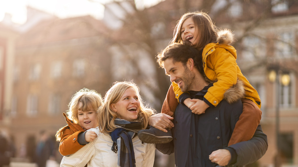 Glückliche Familie spaziert in der Stadt, Eltern nehmen Kinder Huckepack.