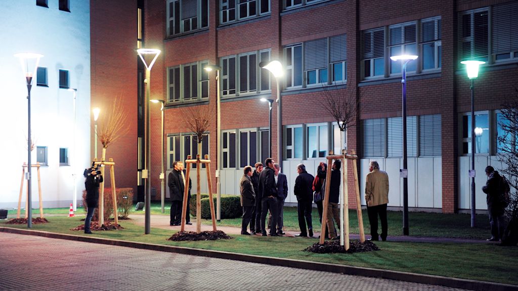 Menschen vor einem Gebäude bei Nacht stehen unter Laternen.