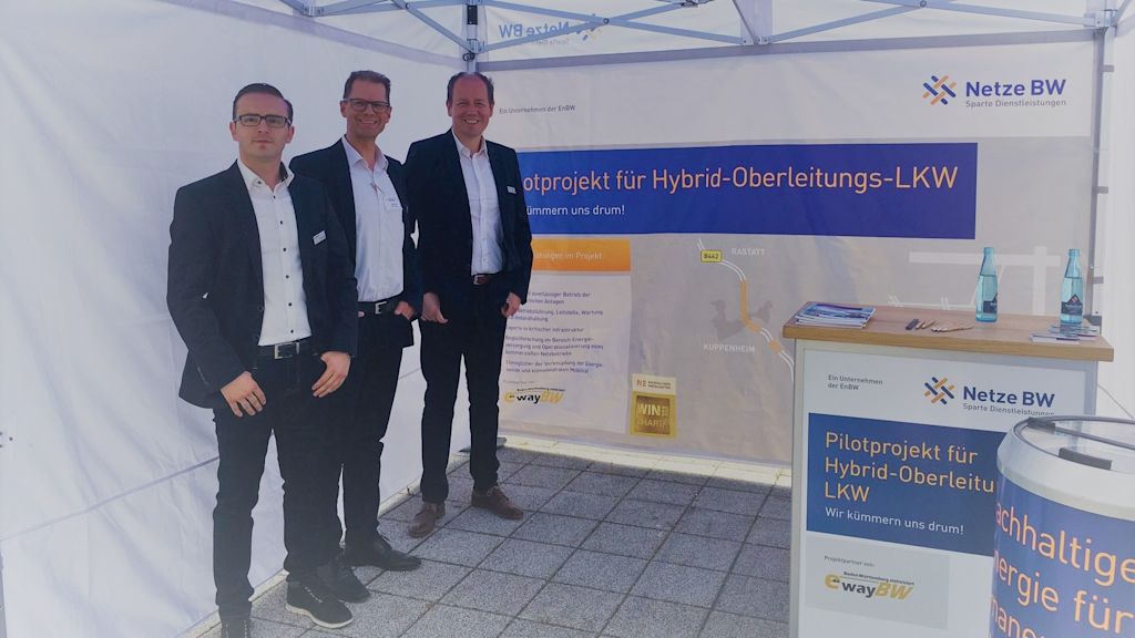 Drei Männer vor einem Netze BW-Stand zum Thema Hybrid-Oberleitungs-LKW.