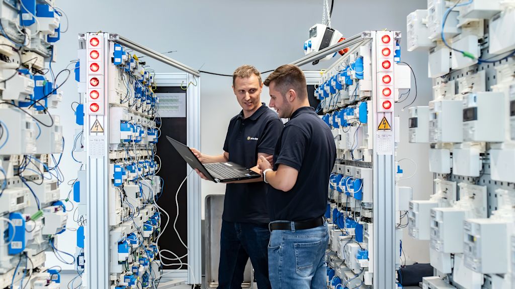 Zwei Techniker prüfen Stromzähler an einem Laptop.