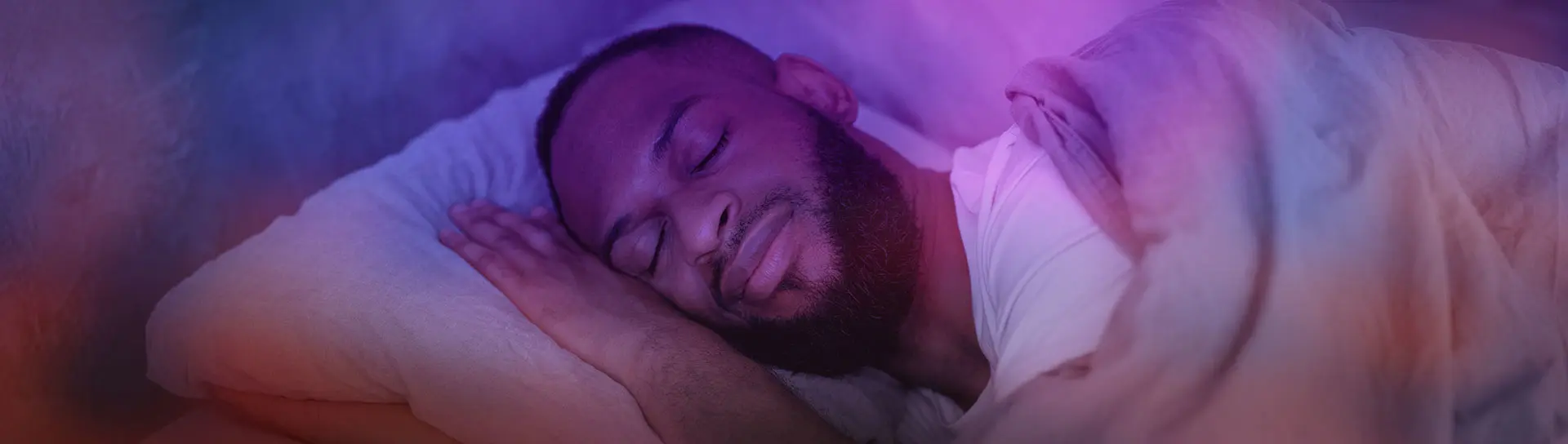 Portrait of young African American man lying in bed with closed eyes, resting in bedroom on the side.