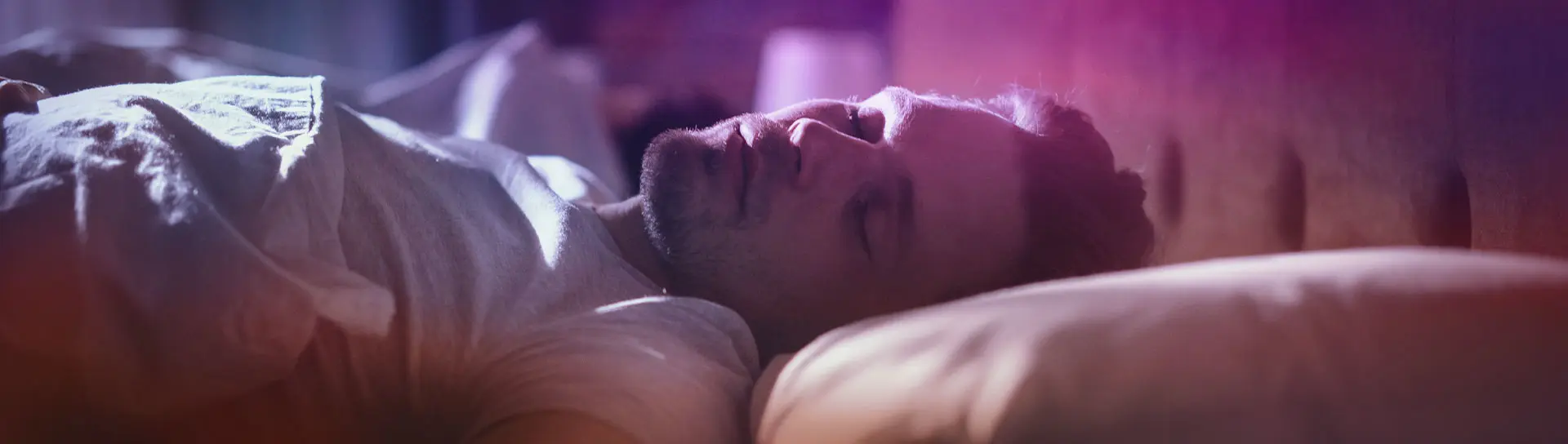 Young man sleeping on a bed, with soft lighting in the room.